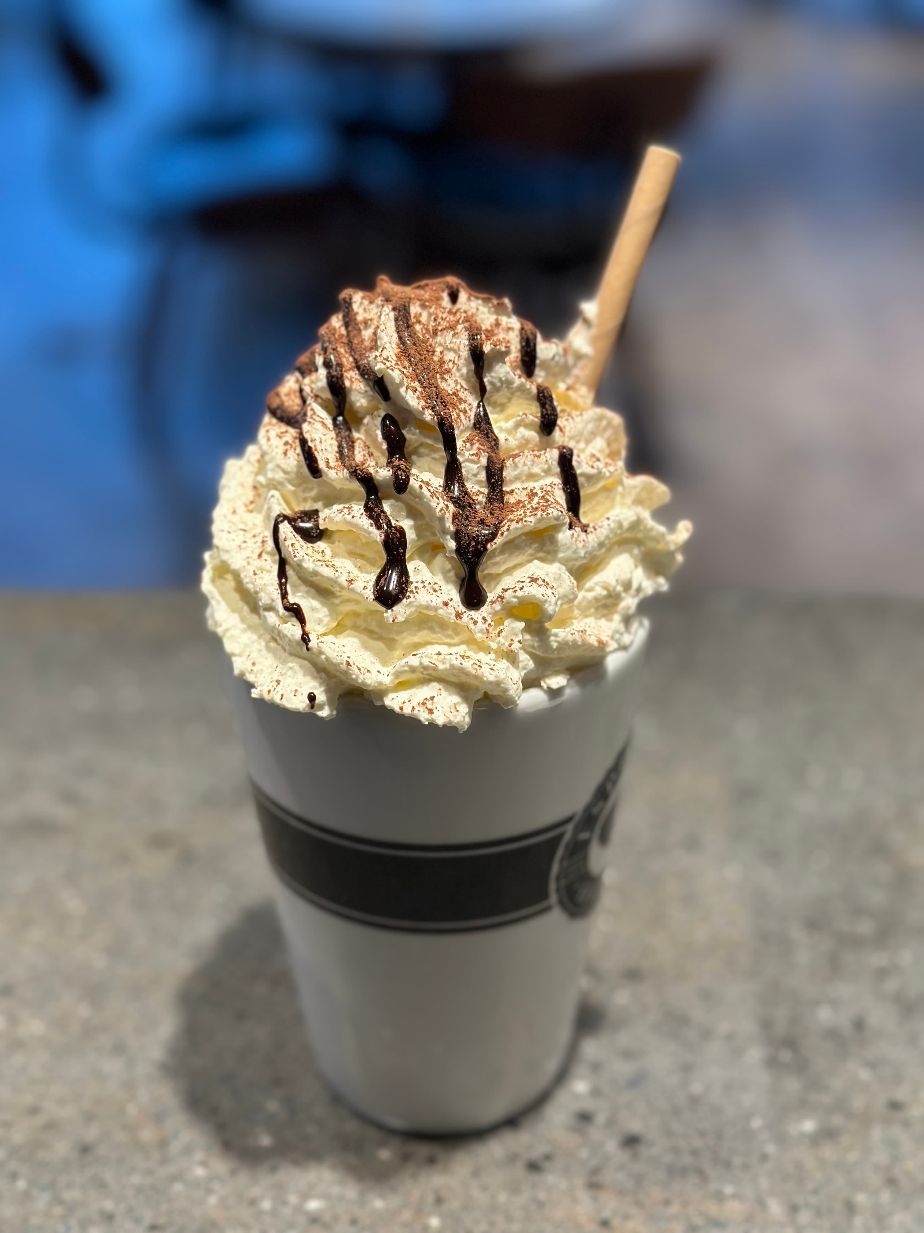 Tall white cup topped with a mountain of whipped cream, chocolate drizzle, and cocoa powder.